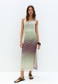 Langes, ärmelloses Kleid in Farbverläufen von Grün und Lila, mit einem drapierten Ausschnitt und seitlichem Schlitz für Bewegungsfreiheit. Der Stoff wirkt weich und fließend.