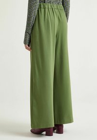 Pantaloni verde a gamba larga con una vestibilità comoda, vita elasticizzata e tessuto morbido; abbinati a stivali con tacco bordeaux dalla texture lavorata.