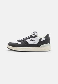 Sneakers Lacoste caratterizzati da una tomaia in pelle bianca e nera, dettagli perforati e una suola in gomma beige. Logo sul lato e sulla linguetta.