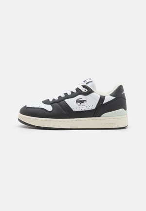 Sneakers Lacoste caratterizzati da una tomaia in pelle bianca e nera, dettagli perforati e una suola in gomma beige. Logo sul lato e sulla linguetta.