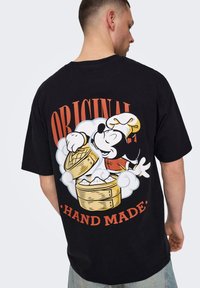 Fekete pamut póló, színes grafikával egy séf követ znajdujával, a szöveg: "ORIGINAL HAND MADE" narancsszínben.