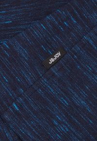 Tissu en tricot marine avec un motif à pois bleus. Présente une étiquette rectangulaire noire avec le texte blanc "J&JOY" brodé. Texture douce.