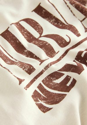 Cotton fabric featuring large, distressed brown lettering on a cream background, with visible texture and slight rippling in the material.