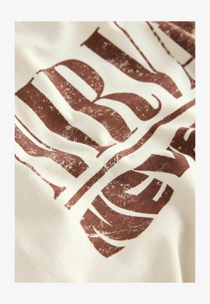 Tessuto di cotone bianco con un design di testo marrone invecchiato. Presenta una tipografia audace e una leggera texture del tessuto, creando profondità visiva.