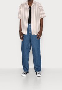 Lyhythihainen raidallinen paita vaaleanbeigeä ja lavenidia, yhdistettynä löysiin sinisiin farkkuihin ja musta-valkoisiin tennareihin.