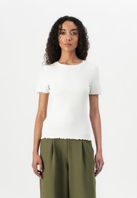 Top bianco a maniche corte a coste con orlo e polsini smerlati, abbinato a pantaloni high-waisted verde oliva. Tessuto liscio, design aderente.
