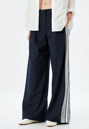 Pantalones de pierna ancha en azul marino, fabricados con una tela suave, que presentan rayas verticales grises a lo largo de los lados. Corte holgado con cintura alta.