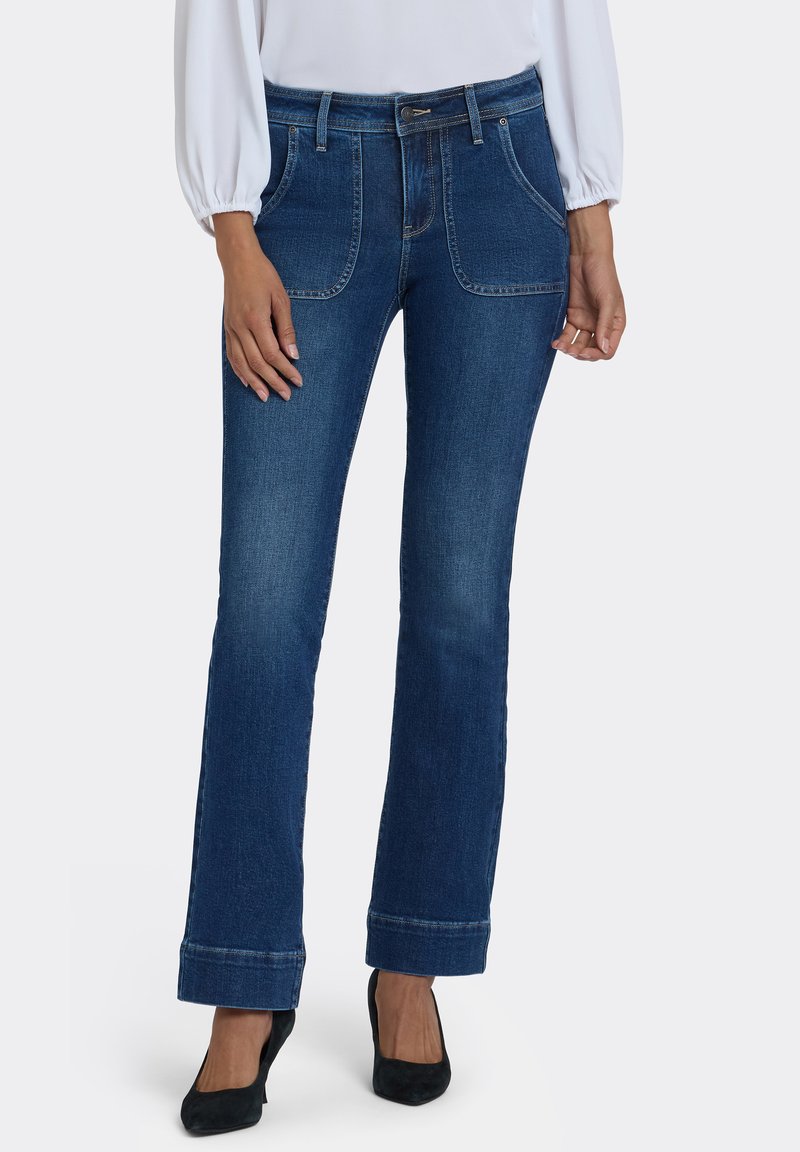 Vaqueros de mezclilla azul oscuro con piernas acampanadas, bolsillos delanteros, trabillas para cinturón y dobladillo enrollado. Textura suave, diseño estándar de cinco bolsillos.