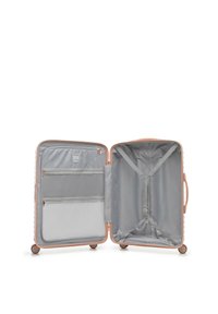 Maleta rígida abierta en oro rosa con cuatro ruedas, con interior gris, bolsillos de malla con cremallera a la izquierda y correas ajustables a la derecha.