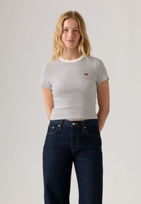 Striped short-sleeve t-shirt in white and navy, featuring a crew neckline and small red logo. Paired with high-waisted dark denim jeans.