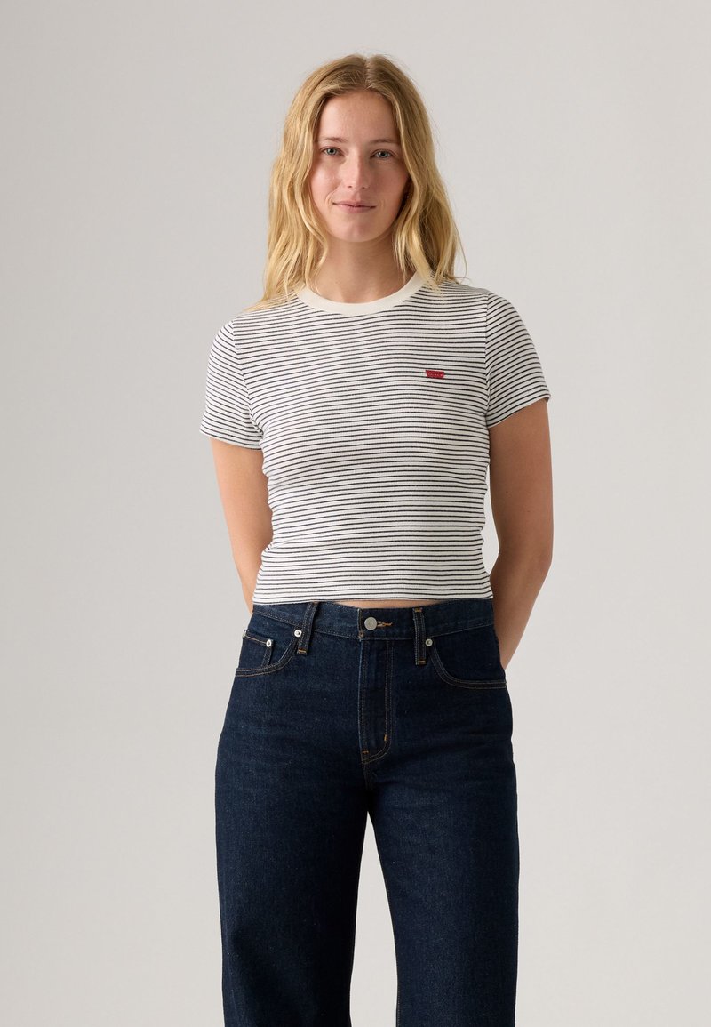 Striped short-sleeve t-shirt in white and navy, featuring a crew neckline and small red logo. Paired with high-waisted dark denim jeans.