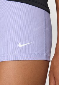Nike athletic shorts in lavender with vertical stripes. Features a white logo on the side and textured fabric with a fitted design.