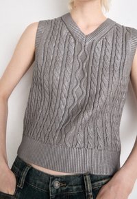 Pull sans manches gris avec un motif torsadé, doté d'un col en V et d'un ourlet côtelé. Le tissu présente une légère brillance et une apparence texturée.