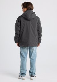 Harmaa huppari, jossa on sileä ja toiminnallinen muotoilu. Yhdistettynä vaaleansinisiin farkkuihin ja tennareihin, nähty takaa.