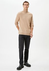 Beige coltrui in een geribbelde textuur, gecombineerd met zwarte recht-toe recht-aan jeans en zwarte enkellaarzen. Minimalistisch, casual ontwerp.