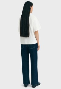 Weißes Baumwoll-T-Shirt und dunkelblaue weite Jeans. Das T-Shirt hat einen lockeren Schnitt, während die Jeans ein klassisches Fünf-Taschen-Design aufweisen.