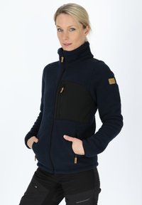 Navy fleece jacket with black chest panel, high collar, zip pockets, and wooden zipper pull. Soft texture, casual fit, and functional design.