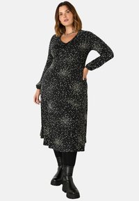 Černé midi šaty s kulatým výstřihem a dlouhými rukávy, zdobené bílým tečkovaným vzorem. V kombinaci s černými vysokými kozačkami.
