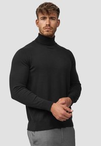 Suéter negro de cuello alto fabricado en un material suave y elástico. Diseño ajustado con mangas largas y bordes acanalados. Simple y versátil.