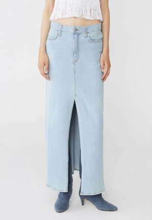 Gonna maxi in denim blu chiaro con uno spacco frontale, cinque tasche, passanti per cintura e chiusura con bottone. Abbinata a stivali alla caviglia grigi.