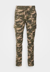 Pantalon cargo camouflage en tons verts et beiges, doté de poches latérales, d’une taille à cordon, de jambes fuselées et de poignets élastiques.