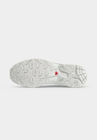 Suola di scarpa bianca con motivo battistrada robusto e piccolo logo triangolare rosso vicino all'arco, mostrata su uno sfondo chiaro e semplice.