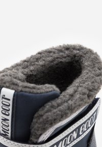 Botas Moon de color azul marino con un suave forro de lana gris, que cuentan con una parte superior acolchada, una marca blanca y detalles texturizados a lo largo del cuello.