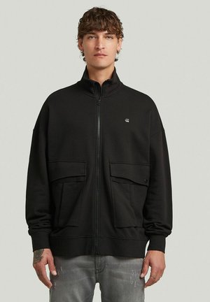 Sweat-shirt zippé noir avec un col montant, comportant deux poches avant et un petit logo sur la poitrine. Matière douce et texturée.