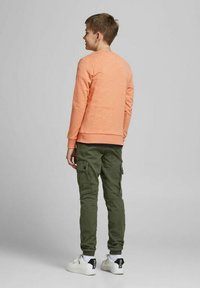 Felpa arancione con maniche lunghe, polsini e orlo a coste, abbinata a pantaloni cargo verde oliva con tasche laterali e sneakers bianche.