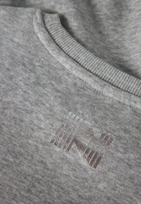 Close-up van een grijze stof met een ribbelhalslijn en een glanzend, reliëf "RN" logo op de borst.