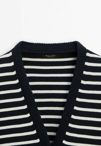 Gros plan d'un pull en maille à rayures horizontales bleu marine et blanc avec un col en V profond et une finition texturée bleu marine.