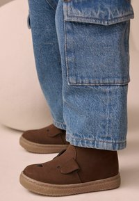 Bruine suède schoenen met een ronde neus, afgewerkt met een flap die op oren lijkt, in combinatie met lichtblauwe denim broeken met cargozakken.