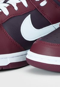 Málo vínové kožené tenisky s bílými akcenty a prošívanými detaily. Obsahují perforovanou špičku a gumovou podrážku pro lepší trakci.