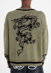 Maglione lavorato a maglia verde oliva con un design di drago nero sul retro, con strisce nere ai polsini e all'orlo. Tessuto testurizzato.