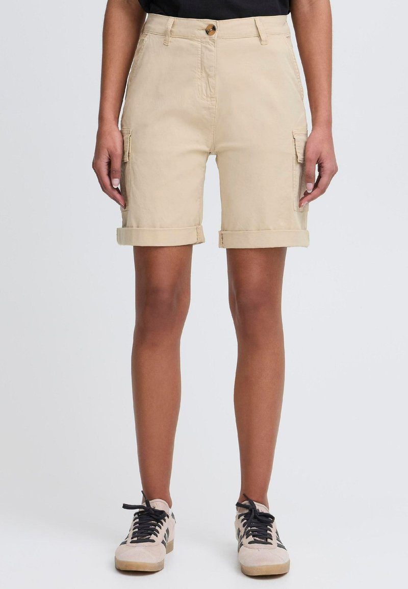 Beige cargo shortser laget av bomull, med rullet manchetter, sidelommer og knappelukking foran. Kombinert med snøresko.