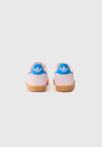 Rosa mockaskinnssneakers med en blå läderhäll och vit logotyp; gummioutsole ger texturerat grepp.