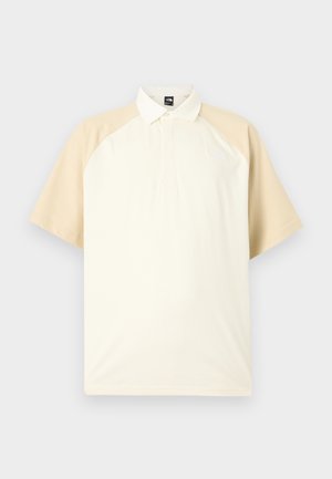 Rövid ujjú, bézs raglán ujjú, krémszínű testű, gombos galléros póló semleges szürke háttéren.