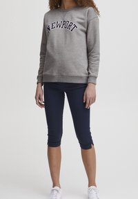 Felpa grigia con scritta "NEWPORT", abbinata a leggings capri blu marina, con un design aderente e sneaker bianchi. Stile semplice e moderno.