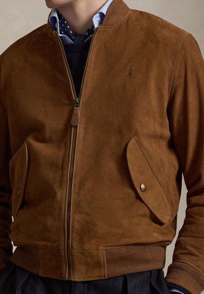 Καφέ σουέντ μπουφάν με φερμουάρ, σε στυλ βομβιστή, με ριμπ μανσέτες και τελείωμα, καθώς και πλαϊνές τσέπες με διακοσμητικά κουμπιά.