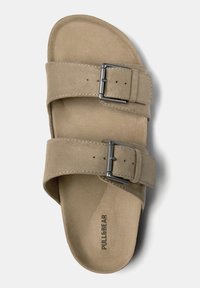 Beige mockasin sandaler med två justerbara remmar med metallspännen, platt sula och präglat varumärke på insidan.
