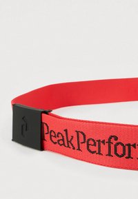 Raudonas audinio diržas su juoda plastmasine sagtimi, ant dirželio juodais siūlais išrašytas užrašas „Peak Performance“. Patvarus ir tekstūruotas dizainas.