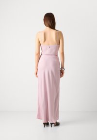 Lungo abito rosa con spalline sottili, vestibilità aderente e un sottile dettaglio sulla schiena. Tessuto liscio e leggero con una silhouette che arriva fino a terra.