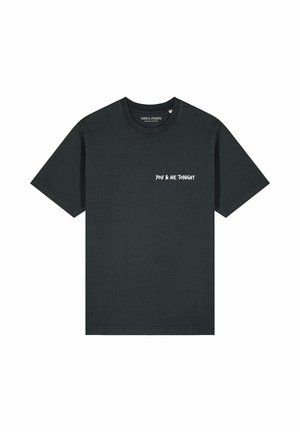 Man draagt een vervaagde zwarte T-shirt met witte tekst "YOU & ME TONIGHT" op de borst, gefotografeerd van de nek tot halverwege de torso.