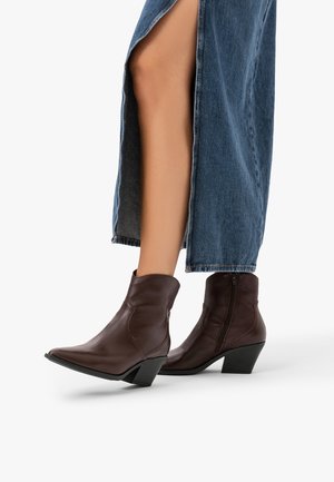 Femme portant des bottines en cuir marron à talons blocs et une longue jupe en denim bleu avec une fente à l'avant.
