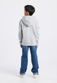 Sudadera gris con capucha ajustable, combinada con jeans de denim azul de corte holgado. Texturas de tejido casual y ajuste relajado.