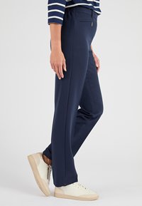 Pantaloni sportivi blu navy con design a gamba dritta, vita elasticizzata e dettaglio con fessura laterale, abbinati a sneakers beige.