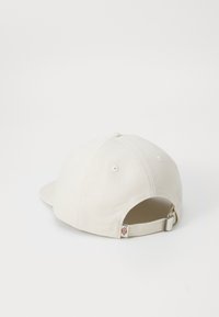 Pamučna bejzbol kapa u boji off-white s zaobljenim vizirjem, šivenim detaljima i podesivom trakom na stražnjoj strani koja ima mali oznaku logotipa.
