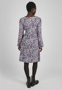 Rochie florală cu mâneci lungi, având un model multicolor pe un fundal închis. Talie ajustată și fustă evazată, asociată cu cizme negre până la gleznă.