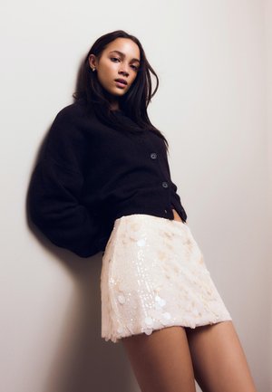 Cardigan nero lavorato a maglia con bottoni, abbinato a una minigonna di paillettes beige chiaro con paillettes tonde e una finitura texturizzata.