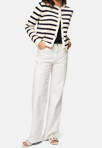 Cardigan à rayures ivoire avec lignes bleu marine, associé à un pantalon blanc taille haute et des sandales légères. Doté de boutons argentés et de poches.